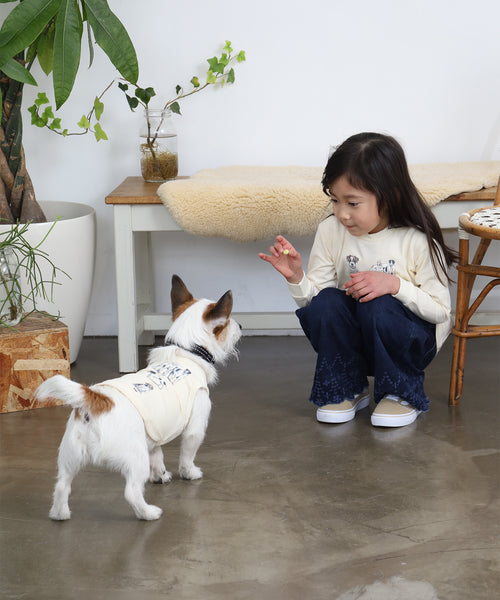 オフホワイトのBritish Dogsキッズ長袖Tシャツを着た子どもが、同じ絵柄のタンクトップを着た愛犬と向き合っているイメージ